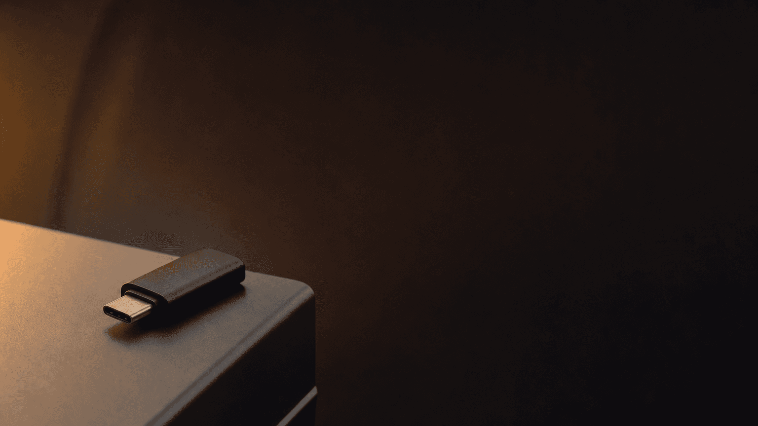 A matte black USB-C drive resting on a Tesla Model S center-console surface with warm amber light spill