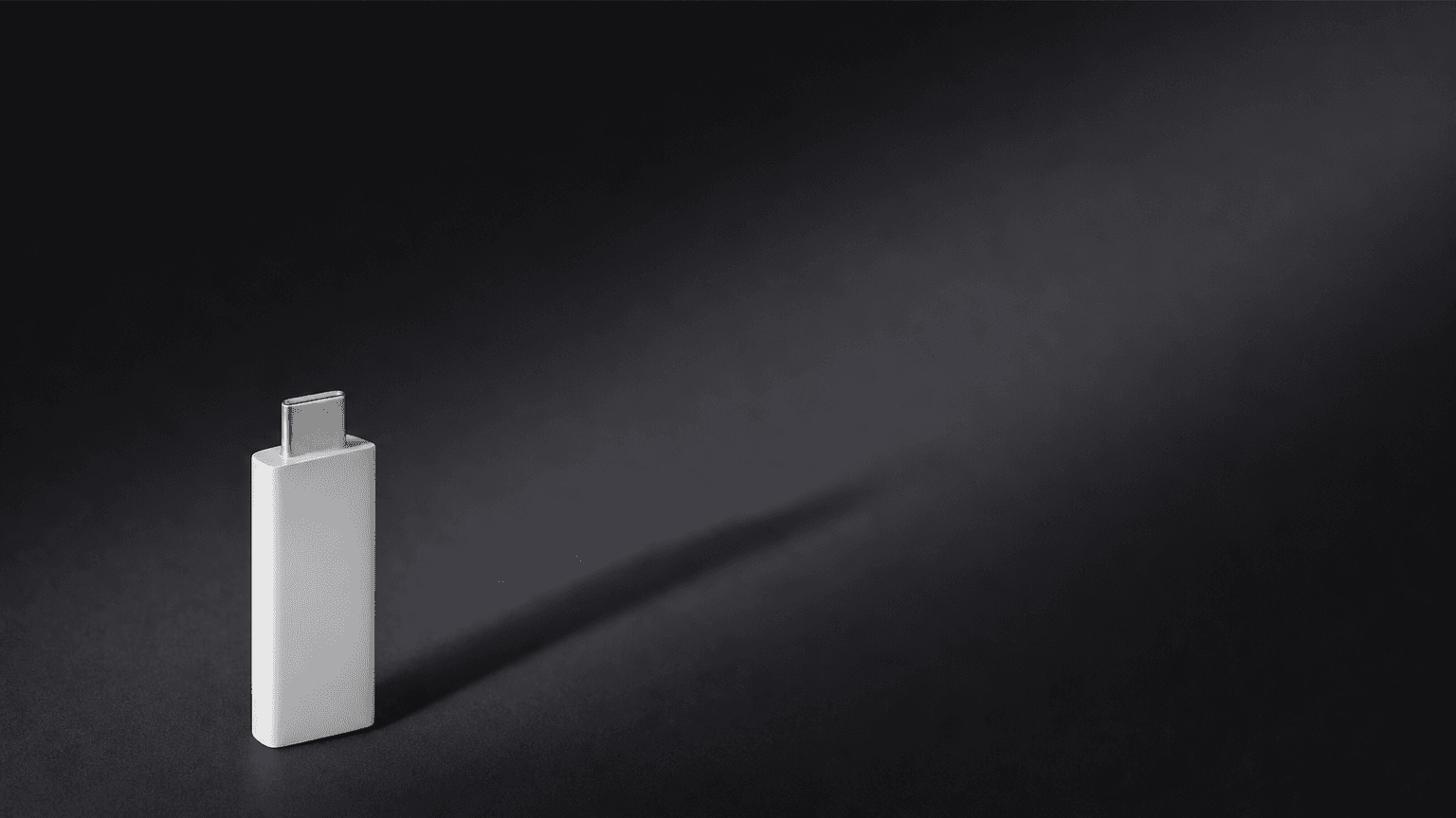 A white USB-C drive standing vertically with a sculptural diagonal shadow, Tesla Model X lock sound install